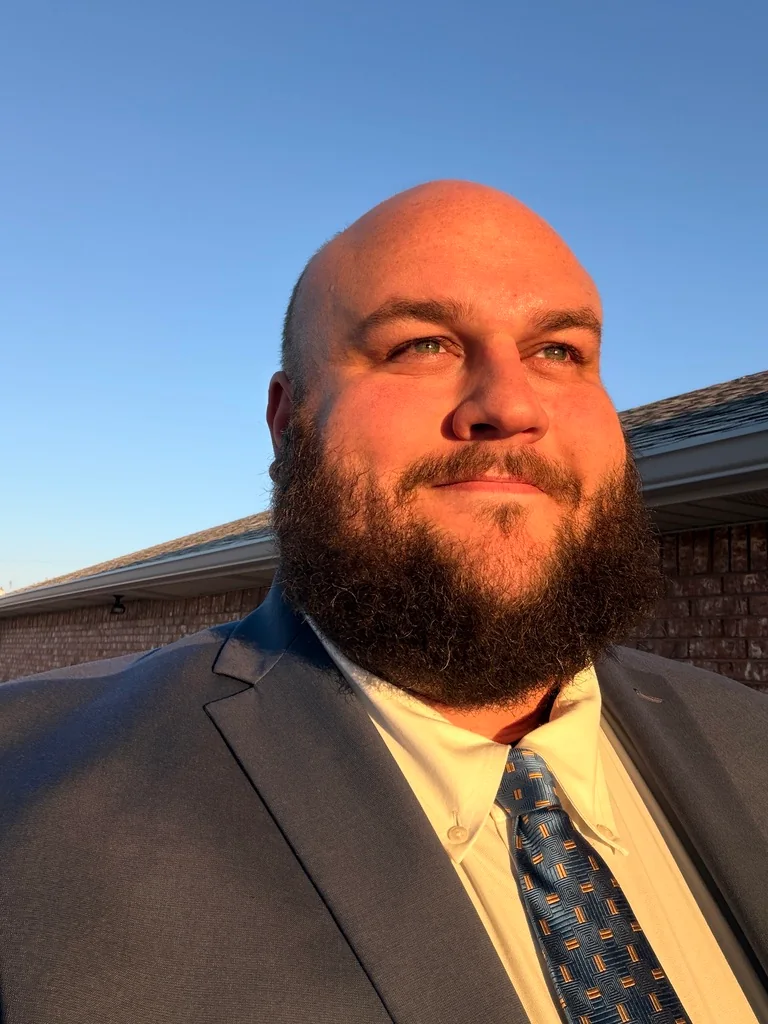 Tom standing outdoors in warm evening light, wearing a suit and tie.